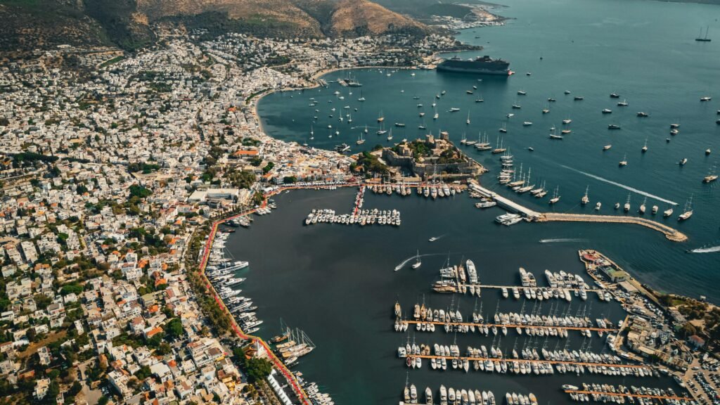 BODRUM – PRIVATE TOUR PROGRAMS Stunning aerial view of Bodrum harbor showcasing numerous yachts and vibrant cityscape under a clear sky.